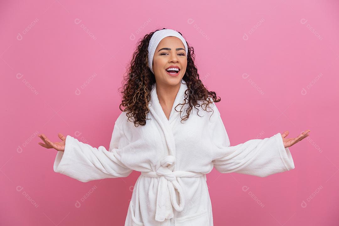 Linda mulher afro, vestida com um roupão de banho, apontando no fundo rosa. mulher afro vestido com poses de manto branco fofo