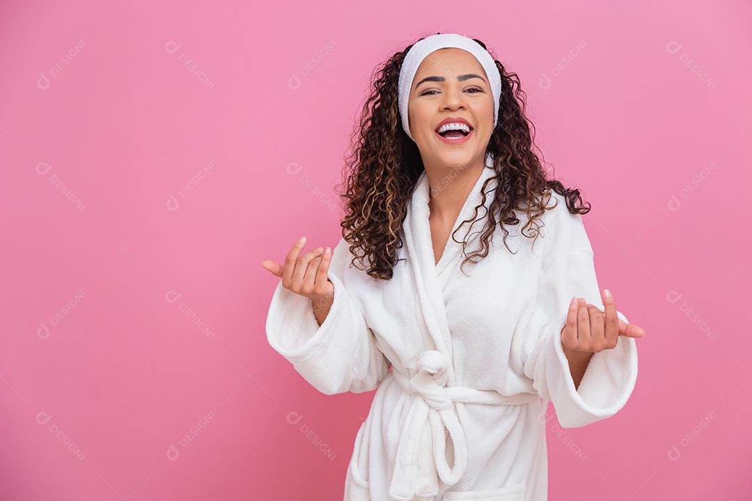 Linda mulher afro, vestida com um roupão de banho, apontando no fundo rosa. mulher afro vestido com poses de manto branco fofo