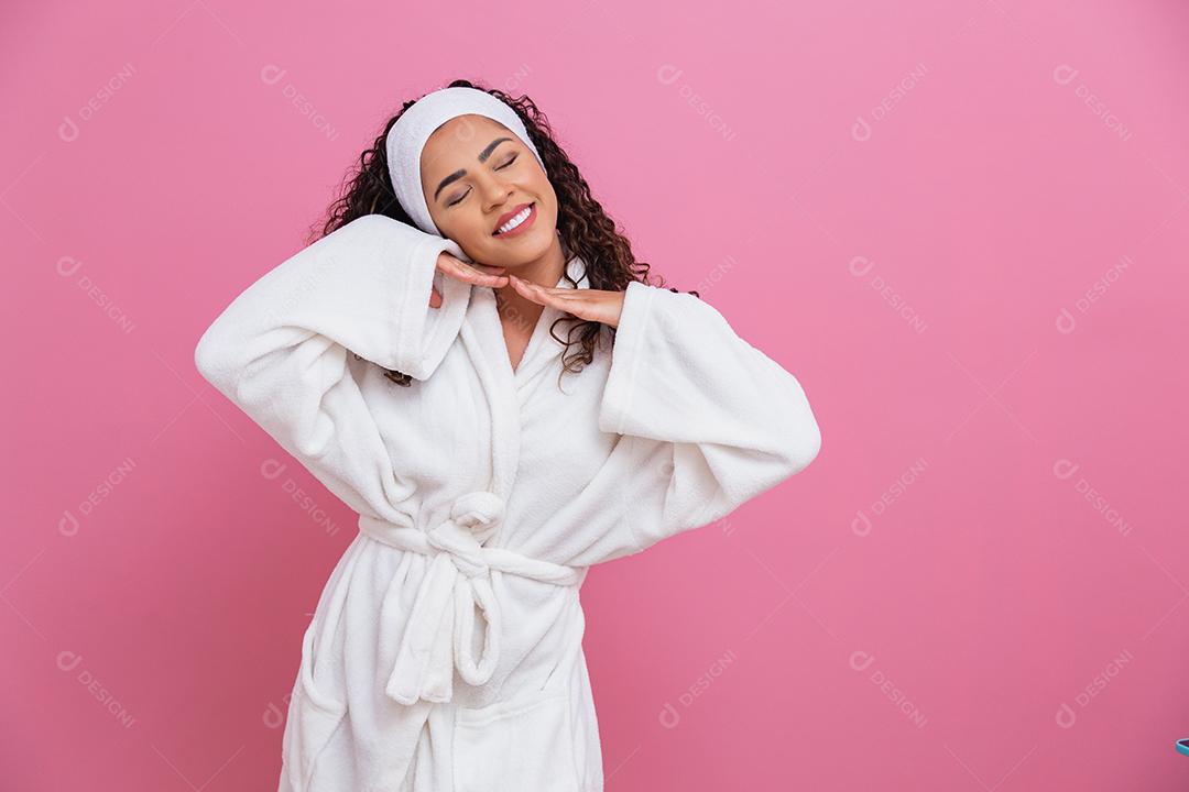 Linda mulher afro, vestida com um roupão de banho, apontando no fundo rosa. mulher afro vestido com poses de manto branco fofo