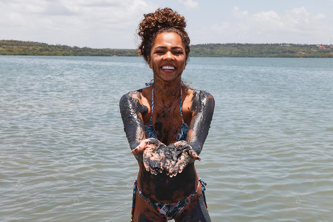 Jovem afro tomando banho em argila natural no rio.