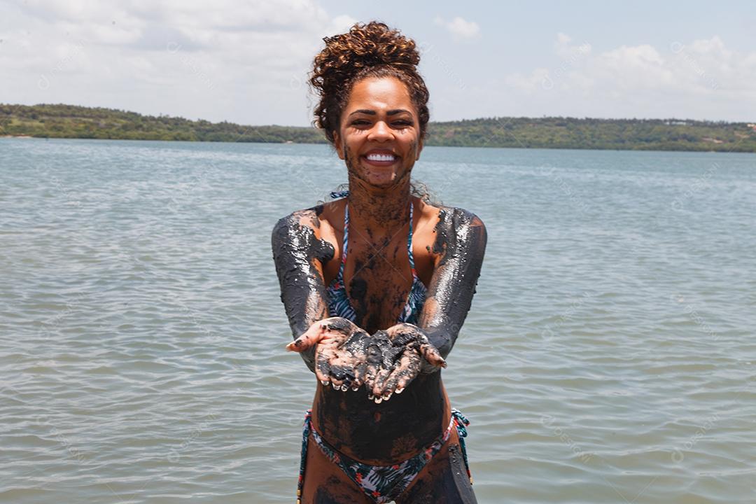 Jovem afro tomando banho em argila natural no rio.