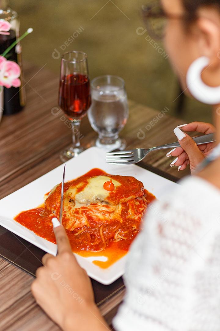 mulher comendo um delicioso prato de carne e macarrão à parmegiana.