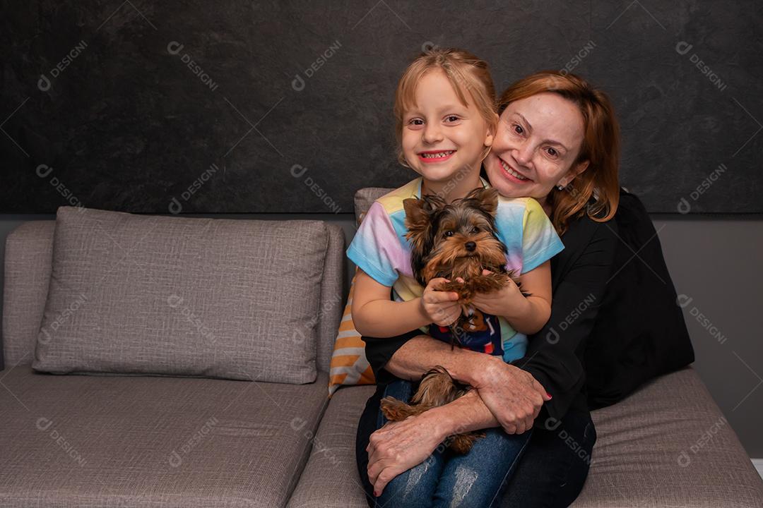 mãe e filha no sofá da sala abraçando seu cachorro