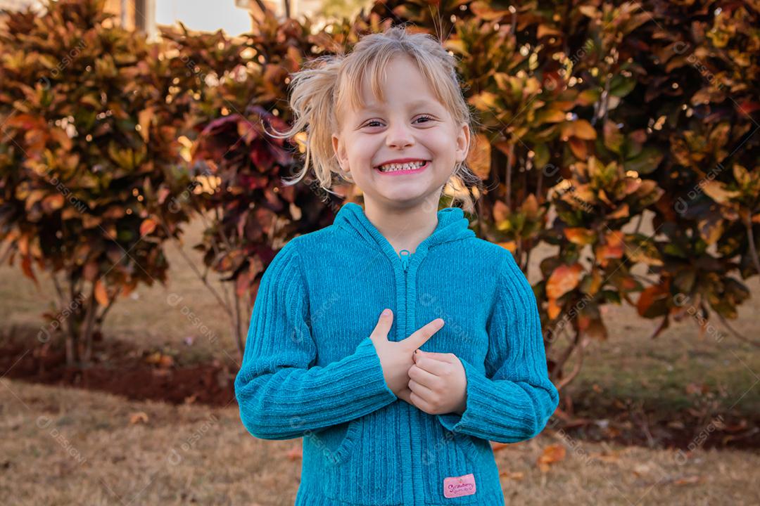 menina criança loira sorrindo para a câmera em suéter frio