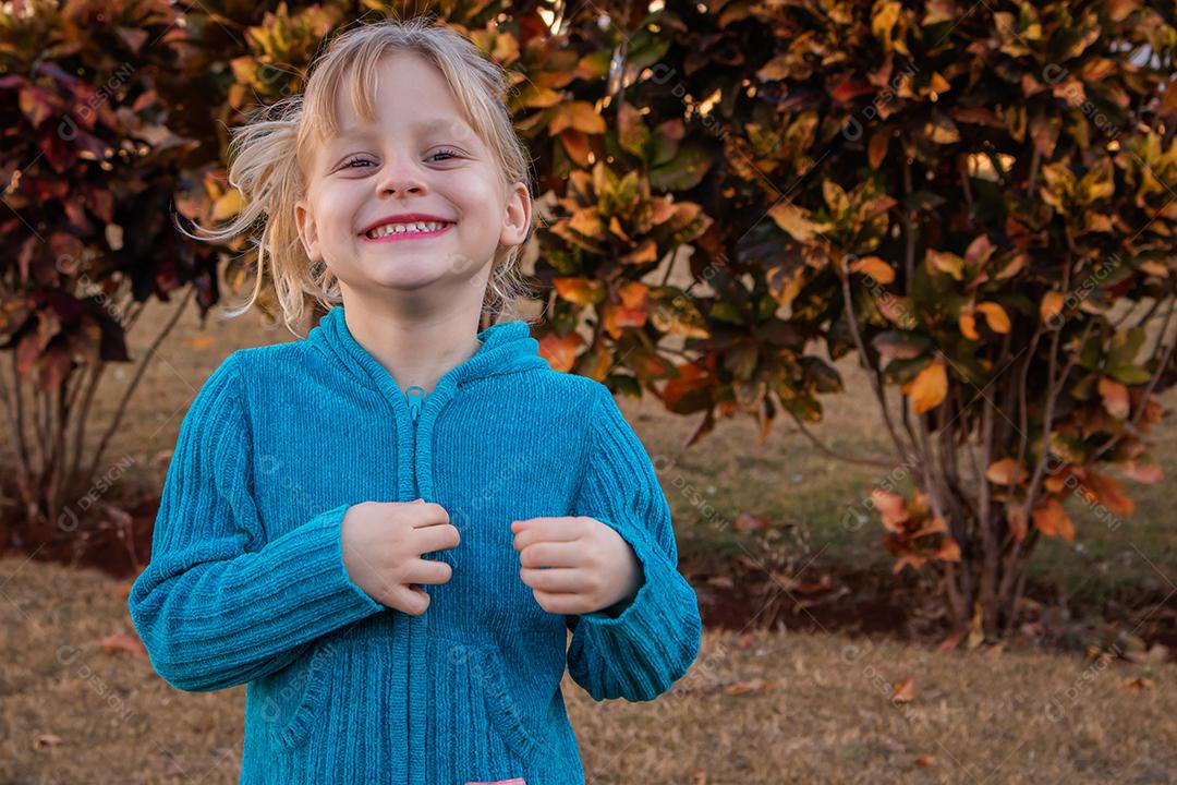 menina criança loira sorrindo para a câmera em suéter frio