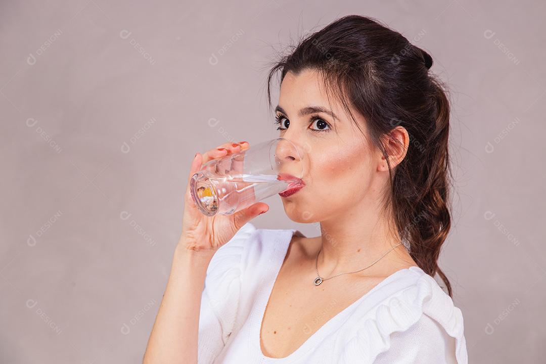Mulher bonita com roupa branca segurando copo de agua em fundo cinza
