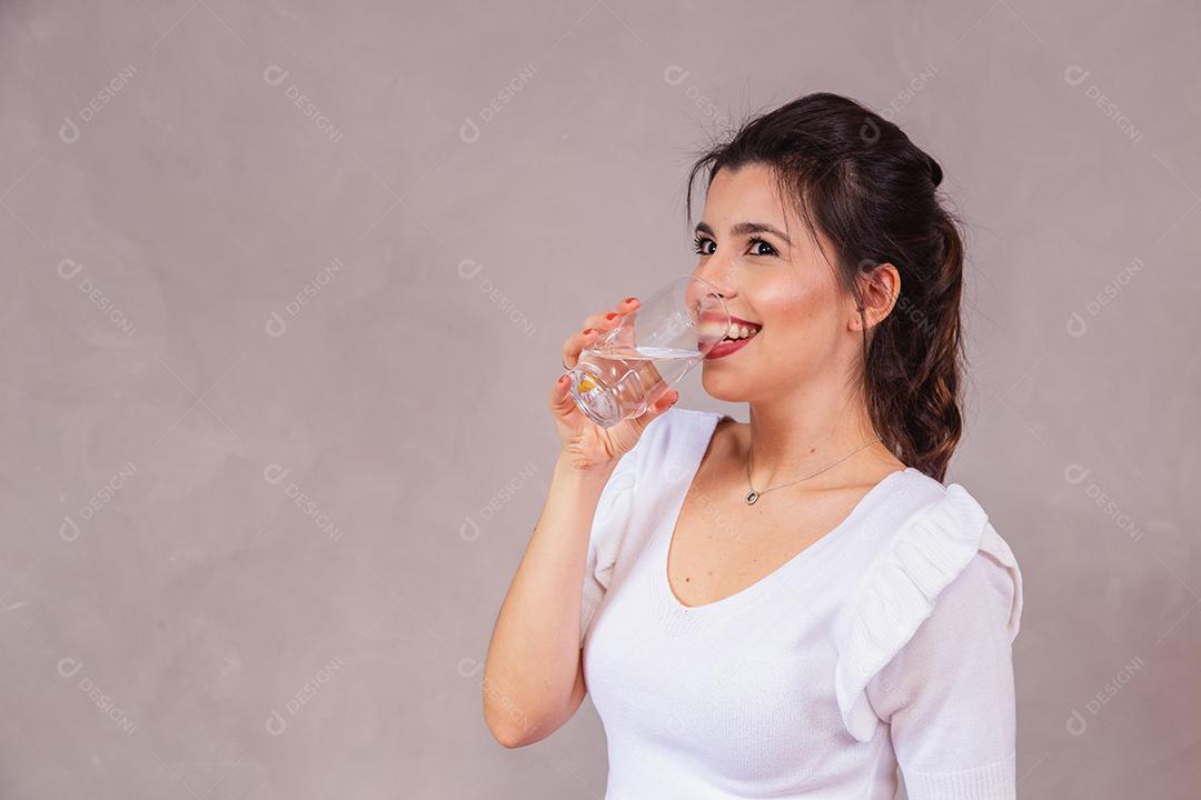 Mulher bonita com roupa branca segurando copo de agua em fundo cinza