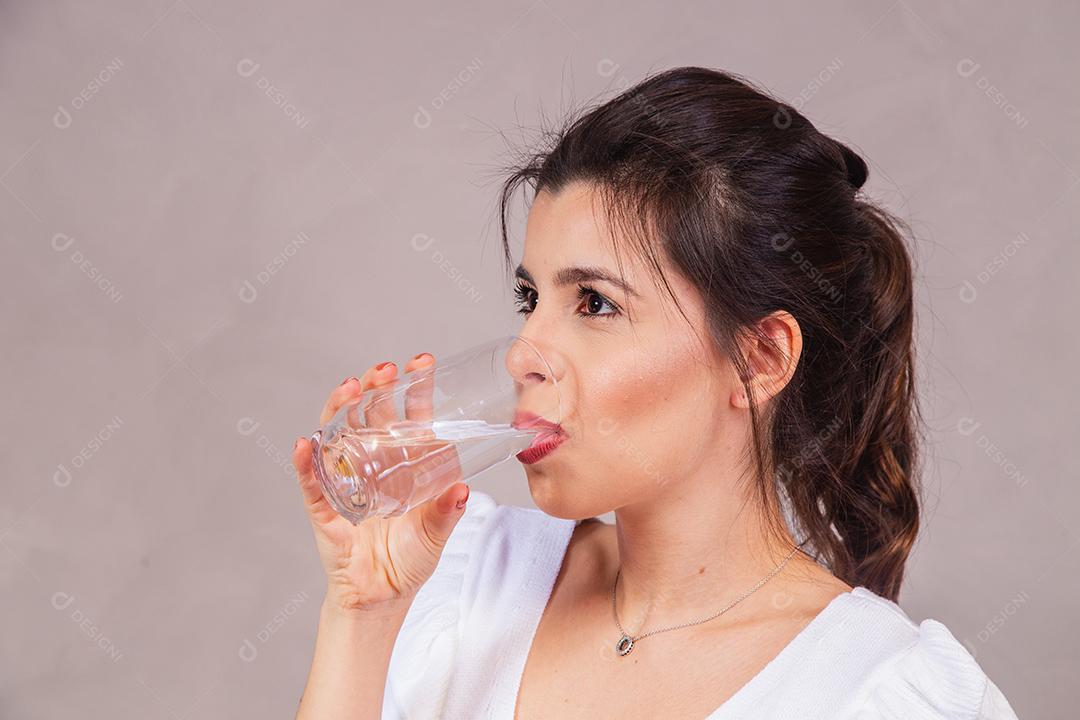 Mulher bonita com roupa branca segurando copo de agua em fundo cinza