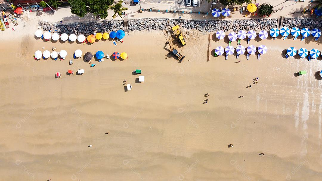 Praia em dia ensolarado com varias pessoas e tendas areia e ondas