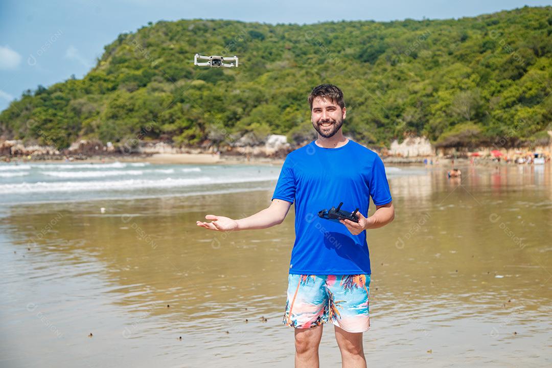 Homem em beira mar praia controlando drone voando em fundo montanhas