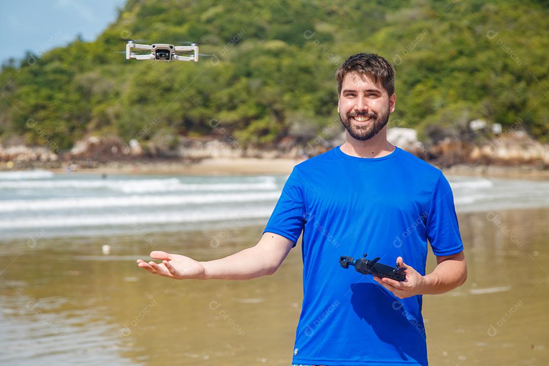 Homem em beira mar praia controlando drone voando em fundo montanhas