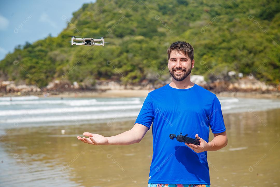 Homem em beira mar praia controlando drone voando em fundo montanhas