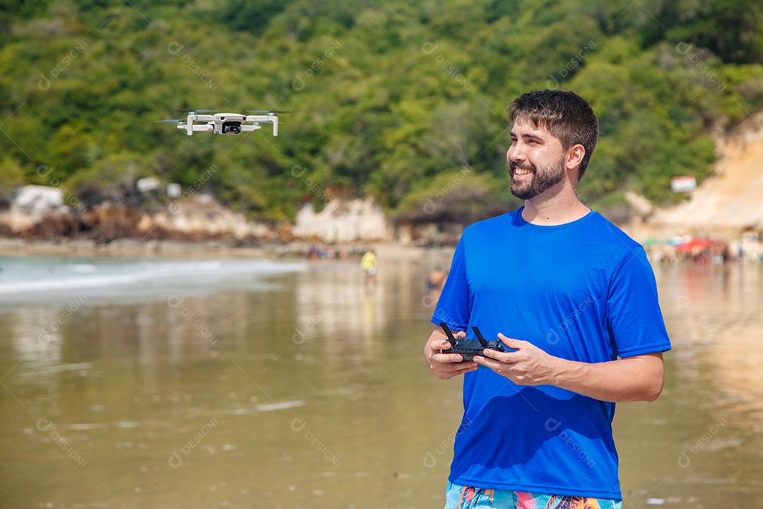 Homem em beira mar praia controlando drone voando em fundo montanhas