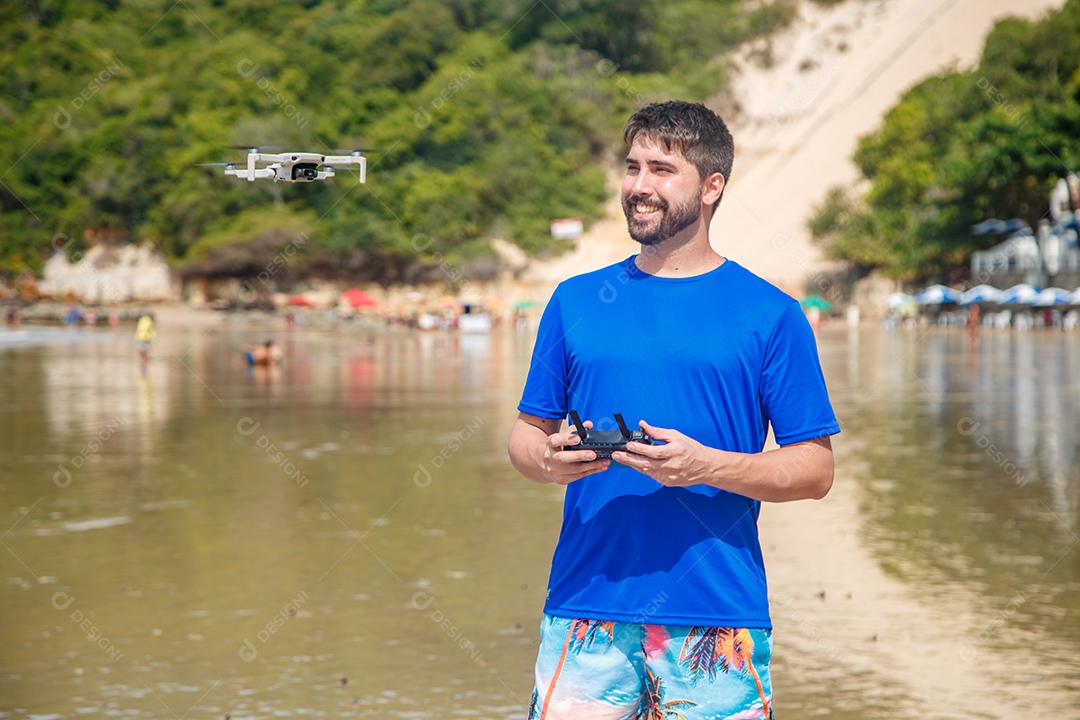 Homem em beira mar praia controlando drone voando em fundo montanhas