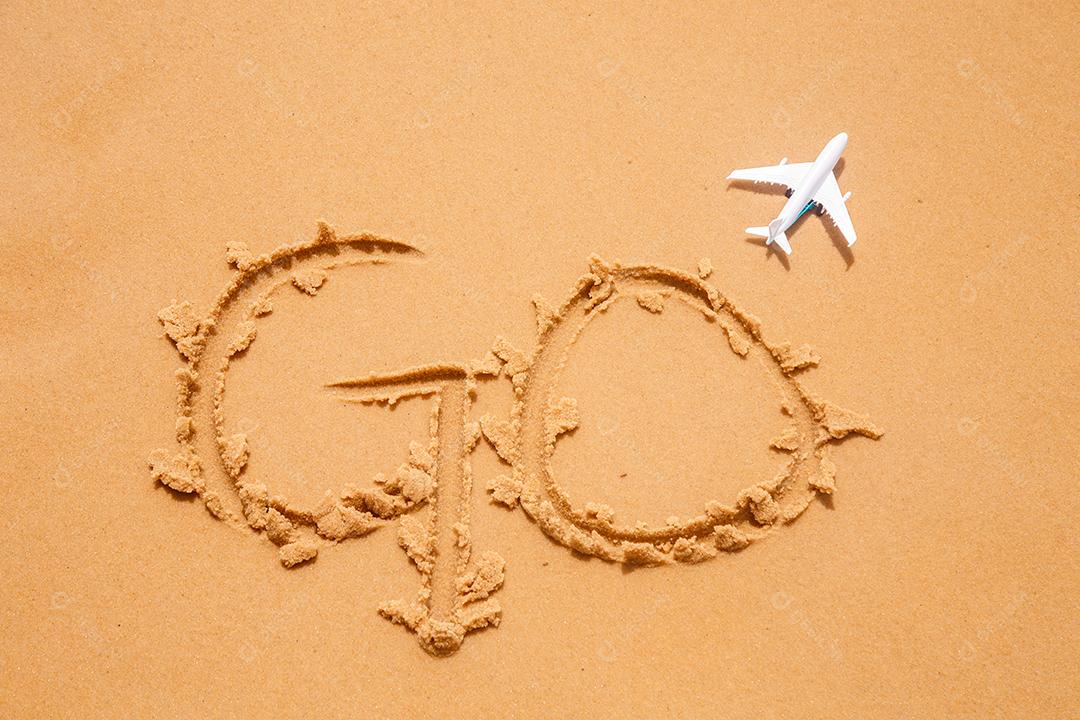 areia da praia escrito go com um avião de brinquedo ao lado. viajar