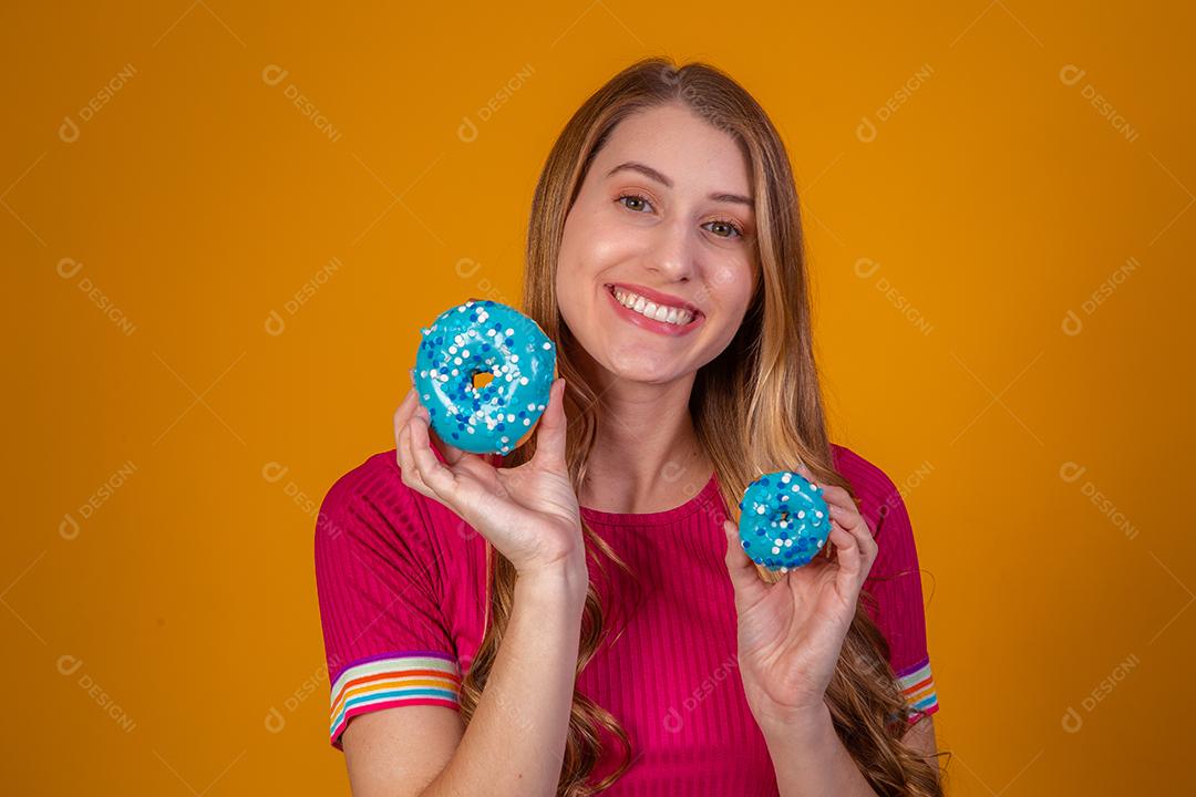 Retrato de uma menina bonita alegre segurando rosquinhas azuis no rosto
