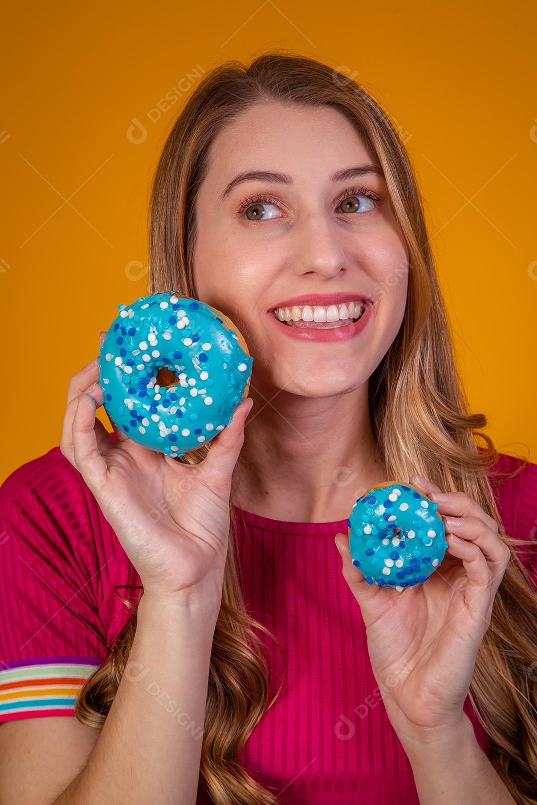 Retrato de uma menina bonita alegre segurando rosquinhas azuis no rosto