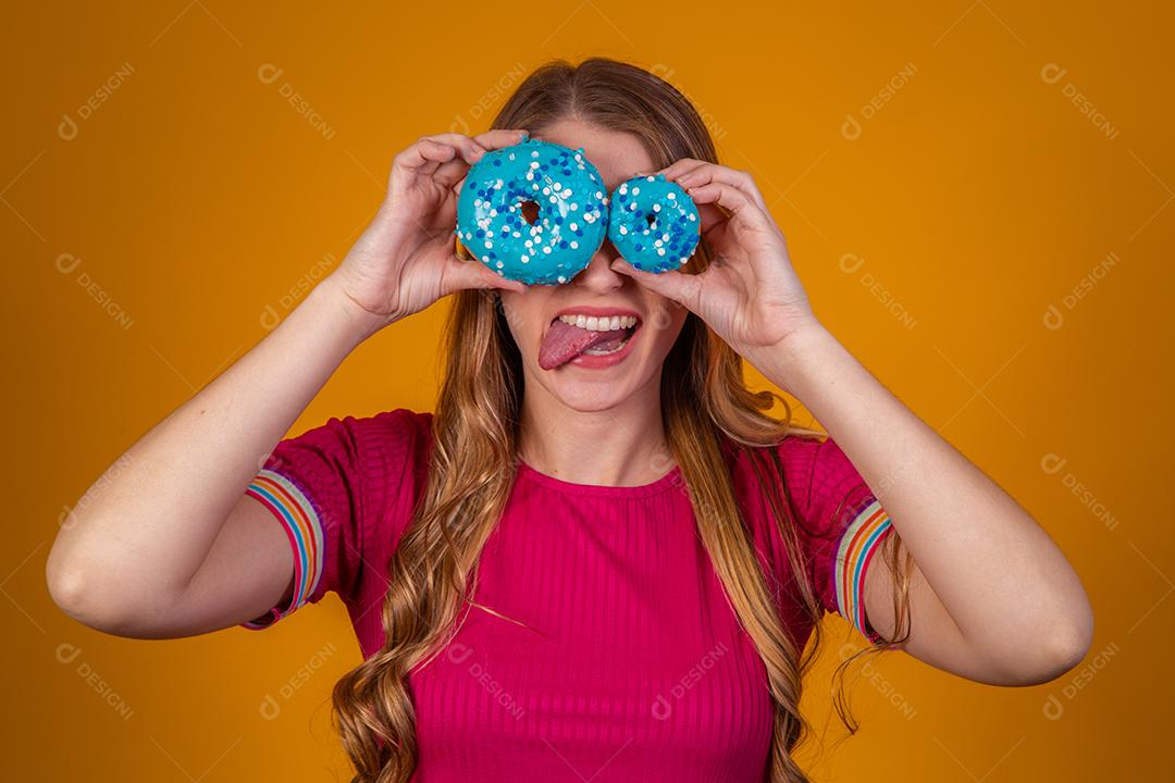 Retrato de uma menina bonita alegre segurando rosquinhas azuis no rosto