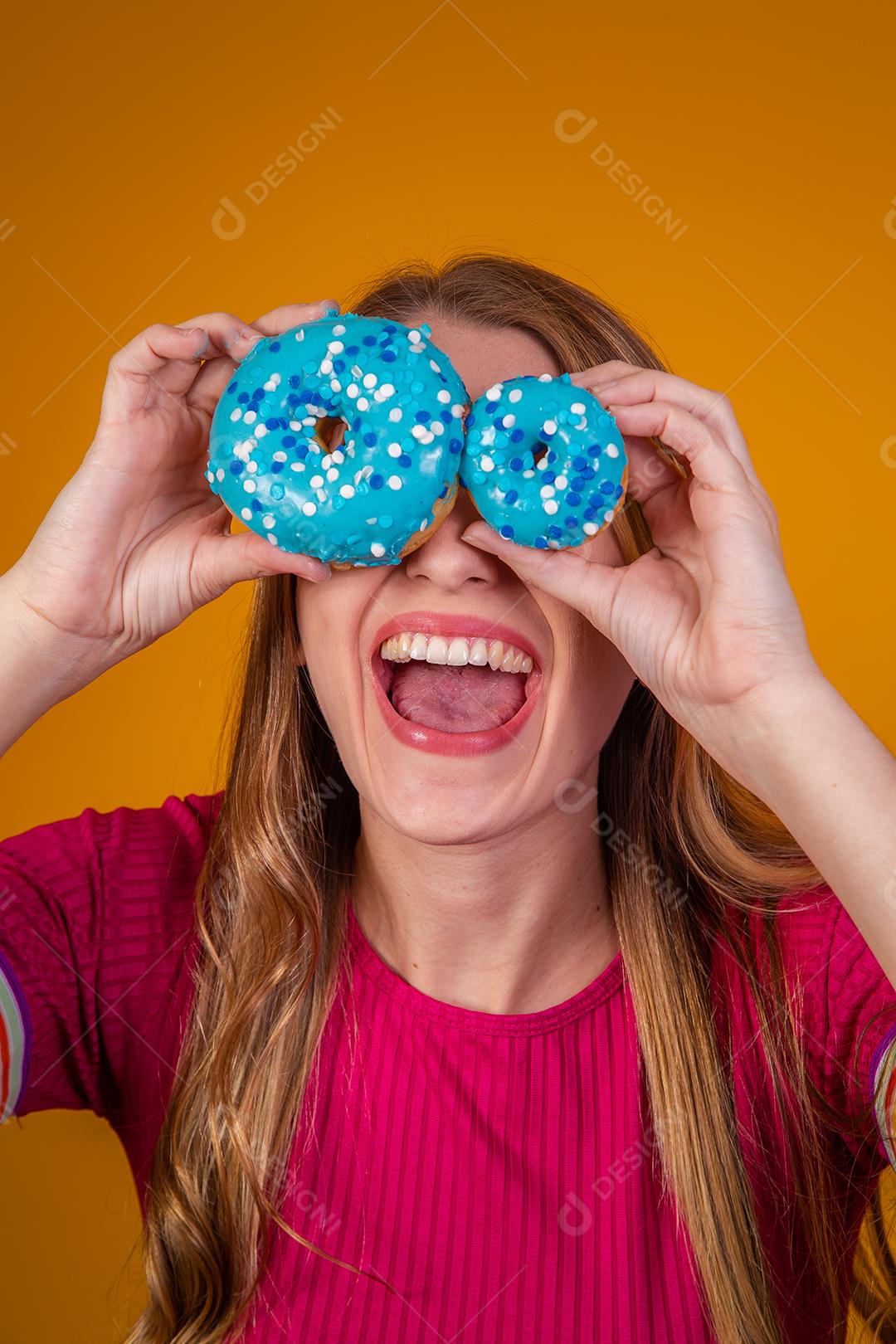 Retrato de uma menina bonita alegre segurando rosquinhas azuis no rosto