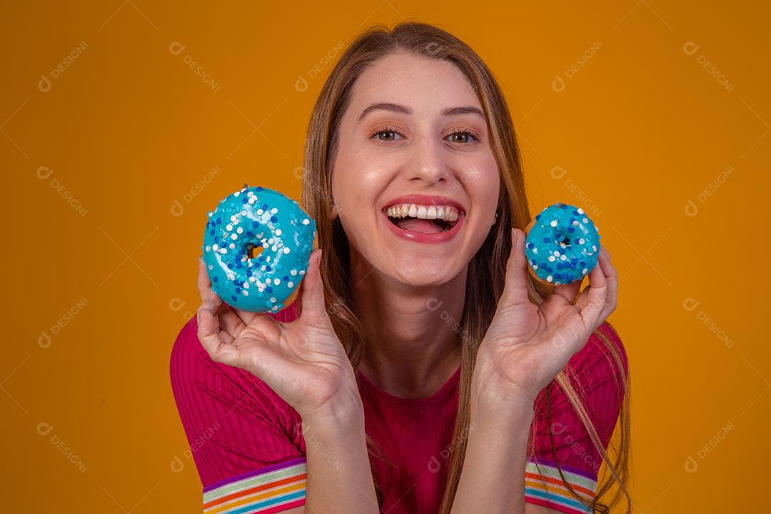 Retrato de uma menina bonita alegre segurando rosquinhas azuis no rosto