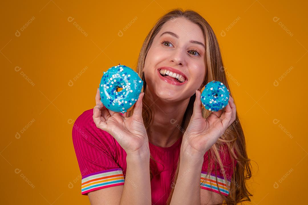 Retrato de uma menina bonita alegre segurando rosquinhas azuis no rosto