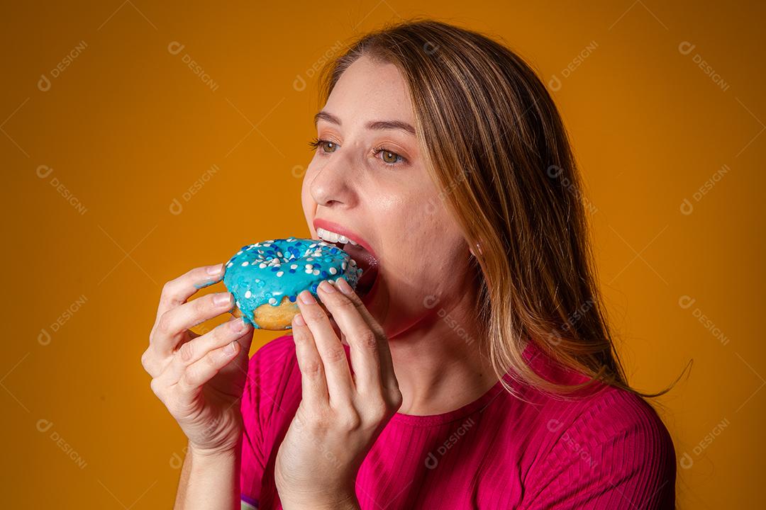 Retrato de uma menina bonita alegre segurando rosquinhas azuis no rosto