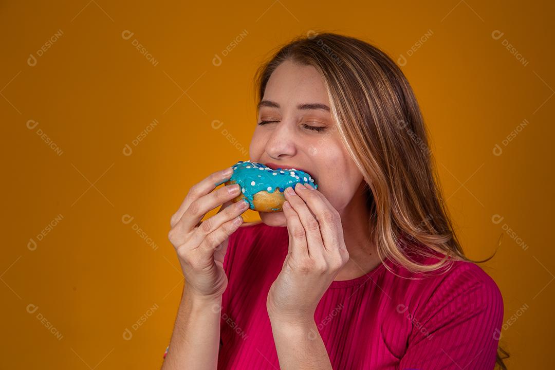 Retrato de uma jovem loira comendo uma deliciosa rosquinha colorida.
