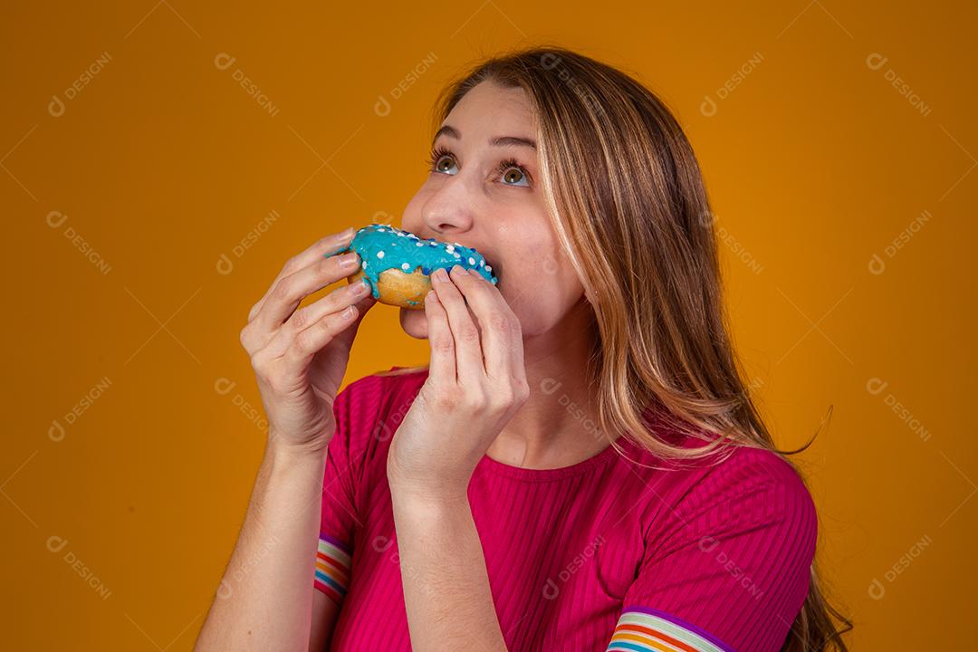 Retrato de uma jovem loira comendo uma deliciosa rosquinha colorida.