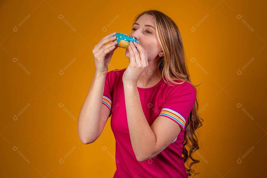 Retrato de uma jovem loira comendo uma deliciosa rosquinha colorida.