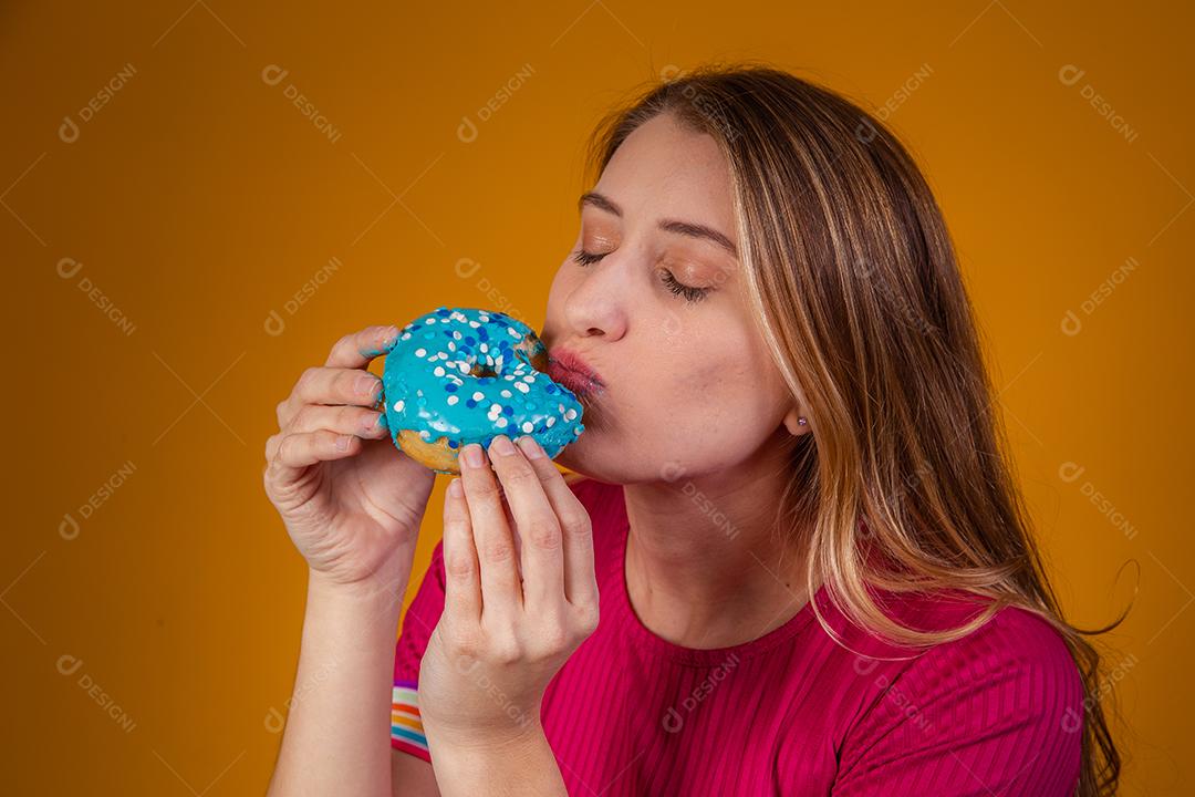 Retrato de uma jovem loira comendo uma deliciosa rosquinha colorida.