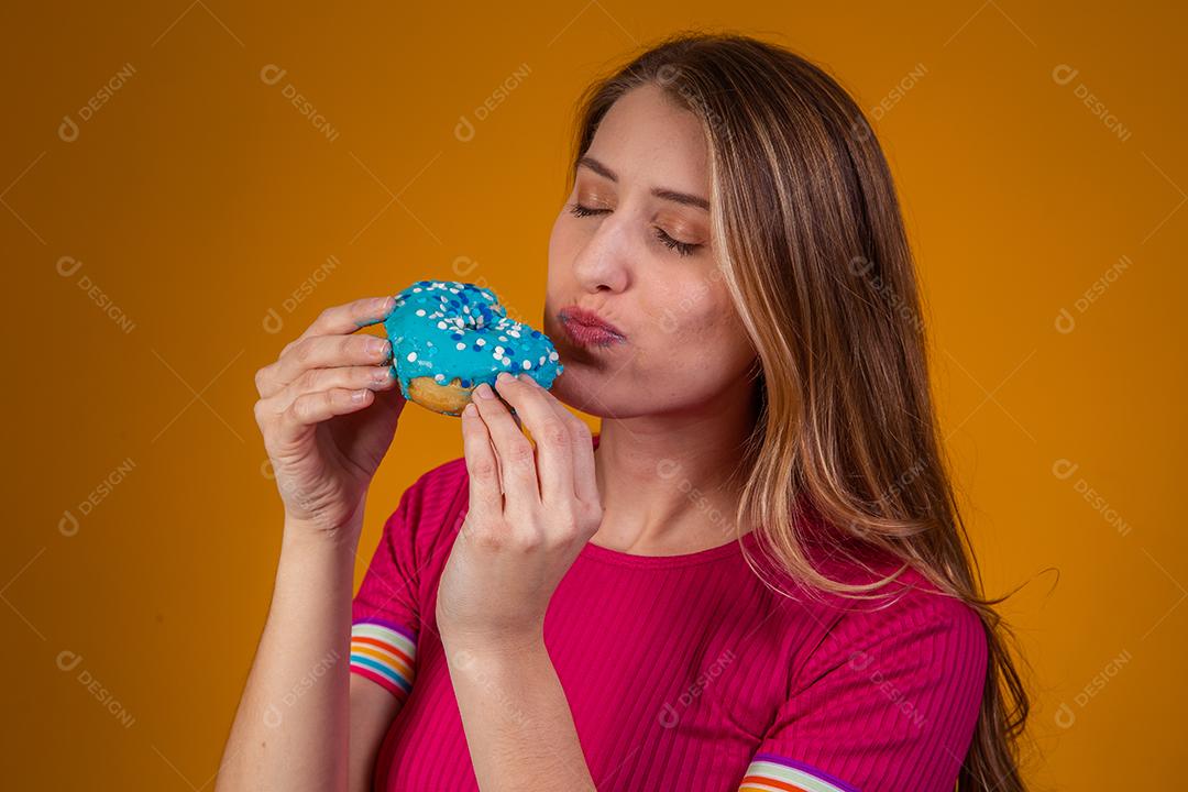 Retrato de uma jovem loira comendo uma deliciosa rosquinha colorida.