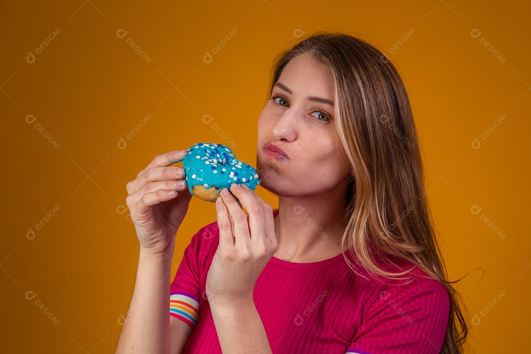 Retrato de uma jovem loira comendo uma deliciosa rosquinha colorida.