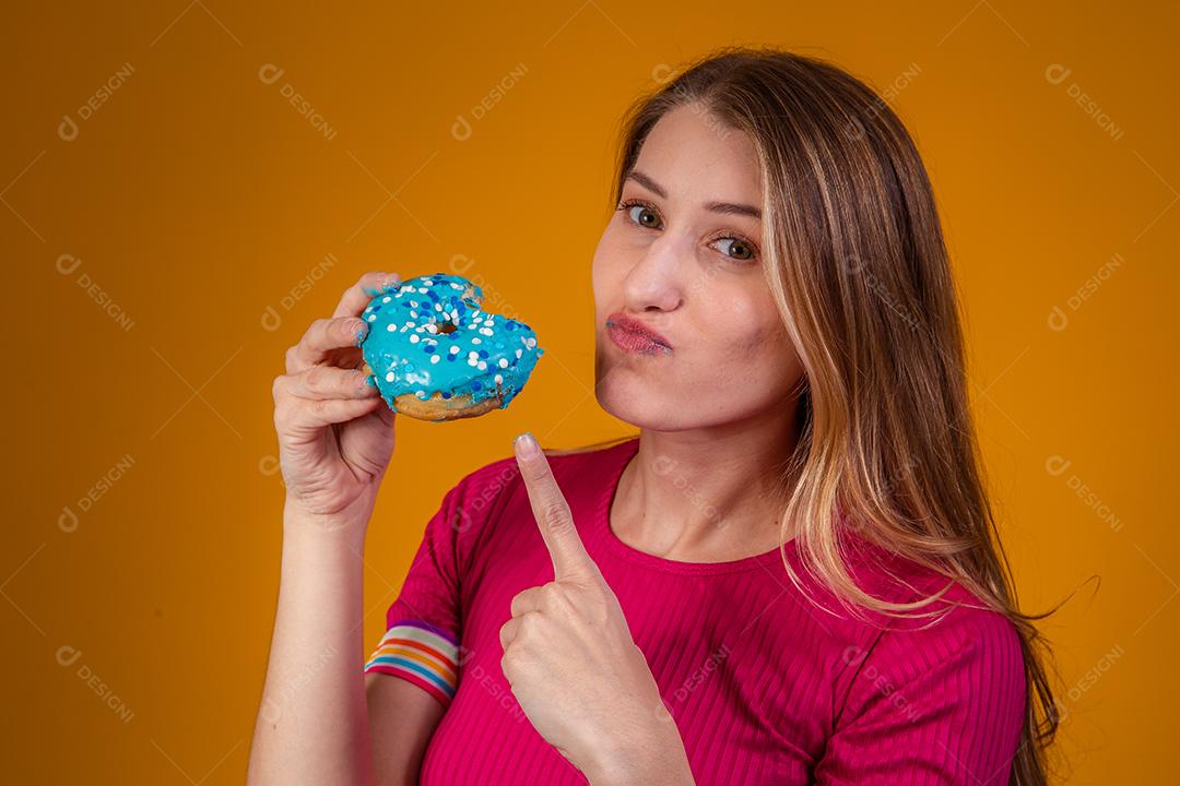 Retrato de uma jovem loira comendo uma deliciosa rosquinha colorida.
