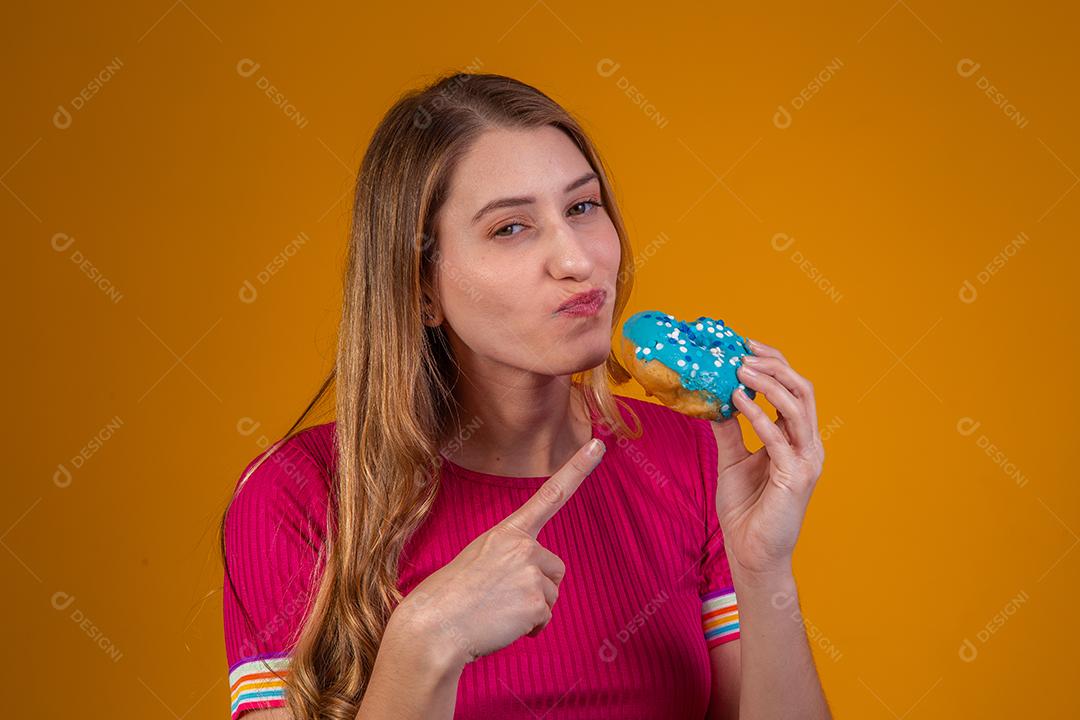 Retrato de uma jovem loira comendo uma deliciosa rosquinha colorida.