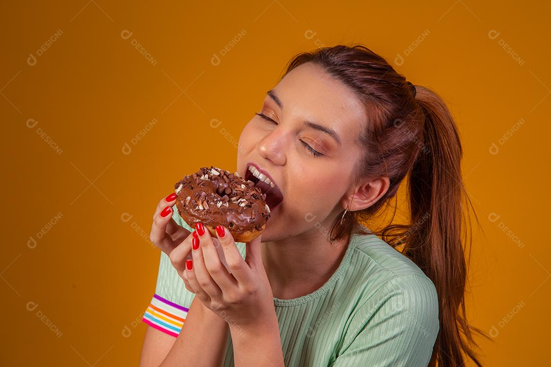 Jovem ruiva comendo deliciosos donuts de chocolate. Jovem desfrutando de rosquinhas saborosas