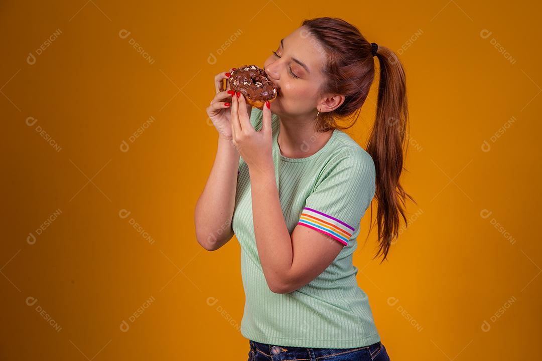 Jovem ruiva comendo deliciosos donuts de chocolate. Jovem desfrutando de rosquinhas saborosas