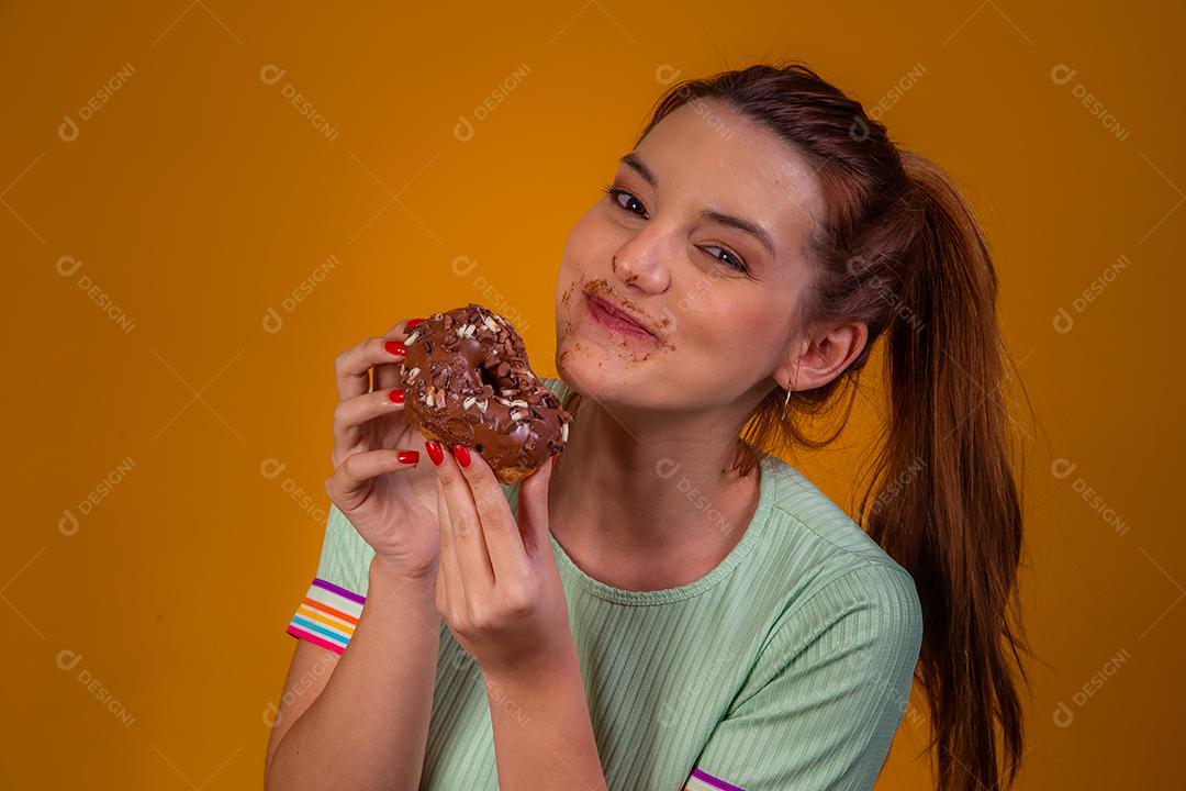 Jovem ruiva comendo deliciosos donuts de chocolate. Jovem desfrutando de rosquinhas saborosas