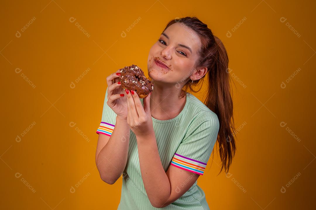 Jovem ruiva comendo deliciosos donuts de chocolate. Jovem desfrutando de rosquinhas saborosas