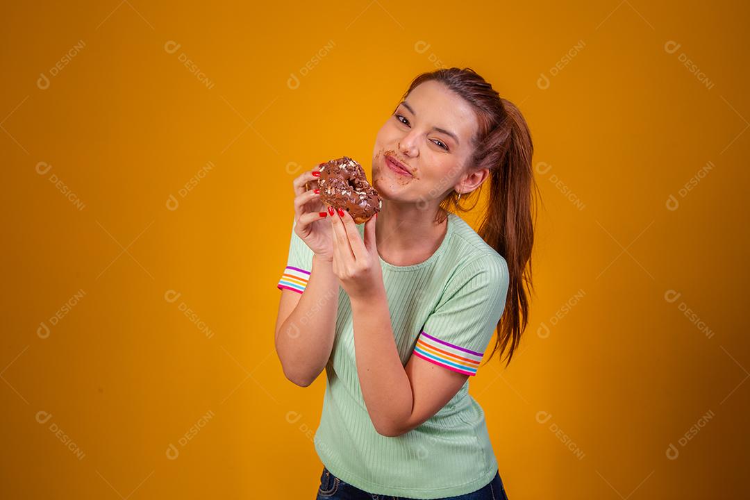 Jovem ruiva comendo deliciosos donuts de chocolate. Jovem desfrutando de rosquinhas saborosas