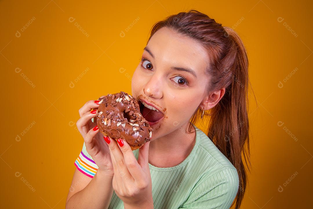Jovem ruiva comendo deliciosos donuts de chocolate. Jovem desfrutando de rosquinhas saborosas