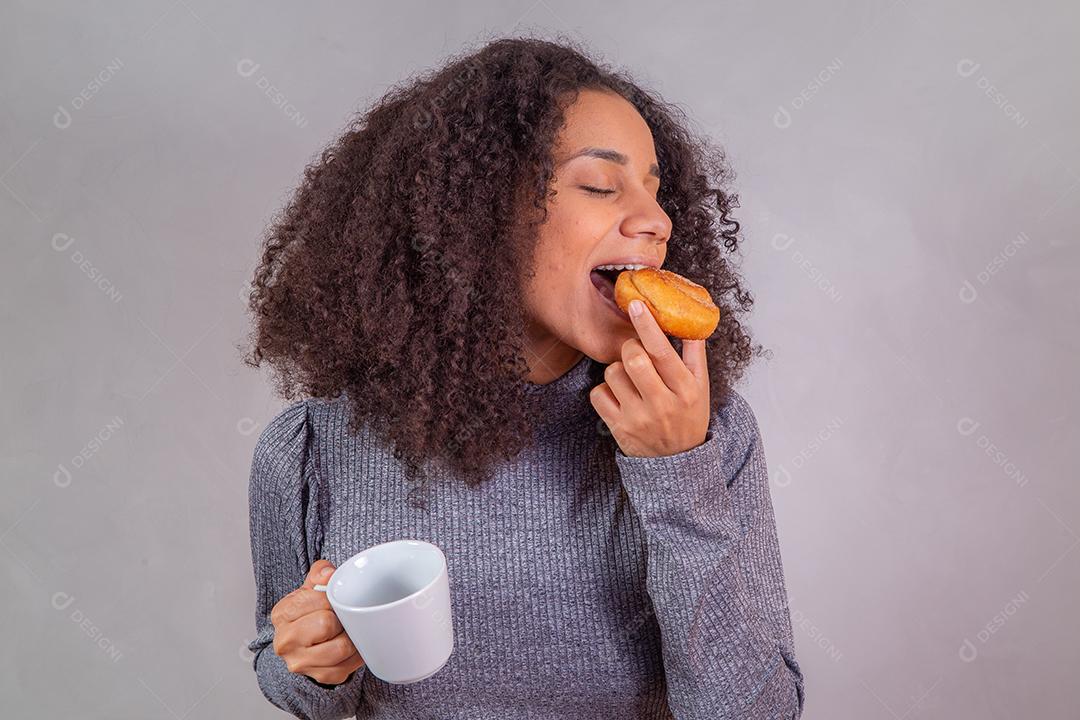 mulher afro comendo rosquinhas e tomando café