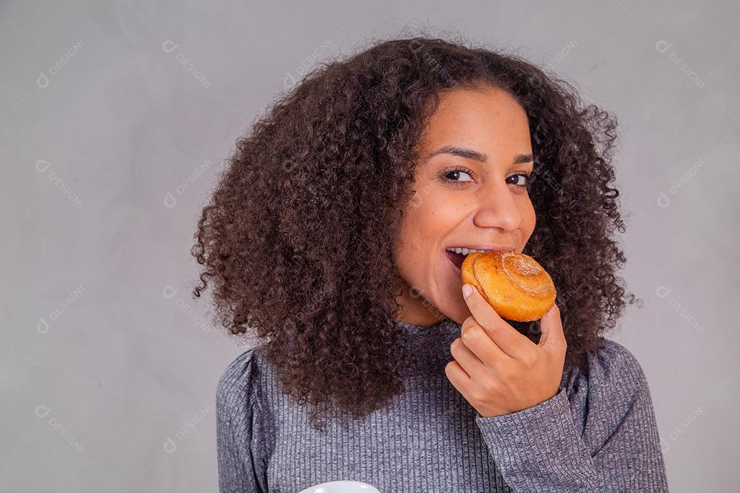 mulher afro comendo rosquinhas e tomando café