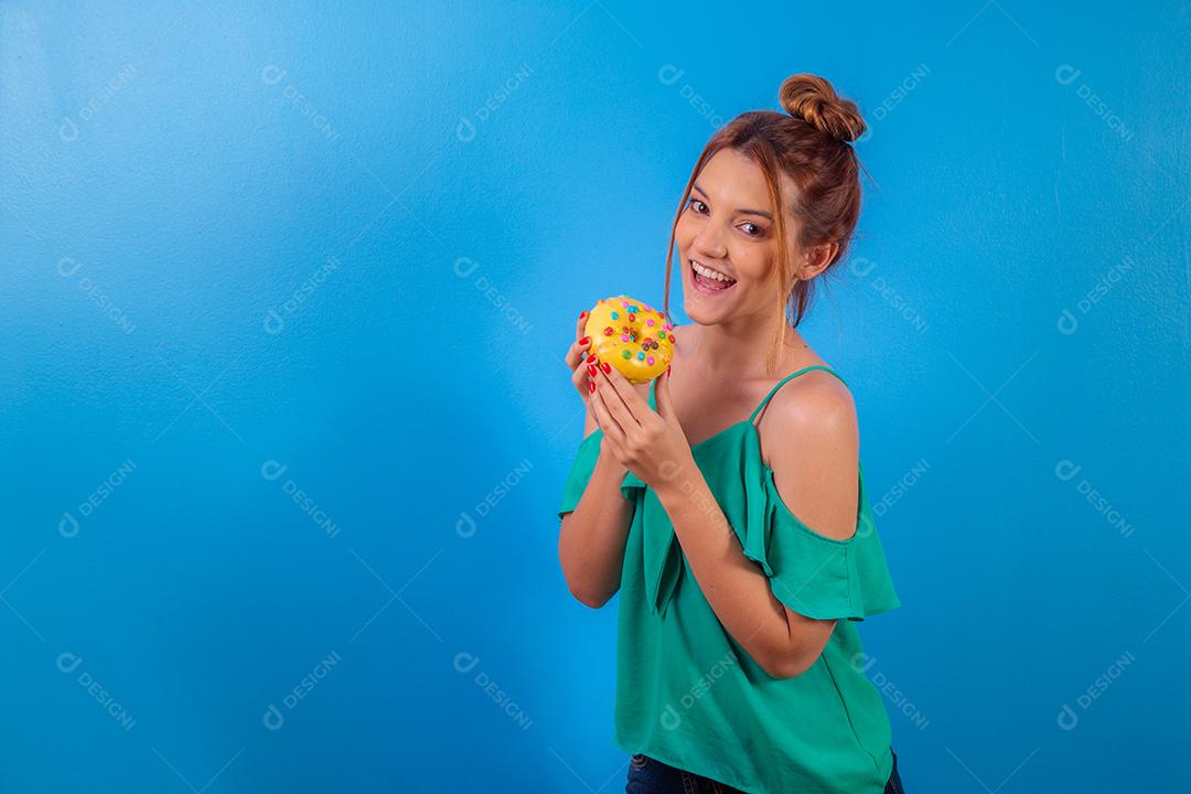 garota ruiva com rosquinha amarela e confetes coloridos sobre fundo azul.