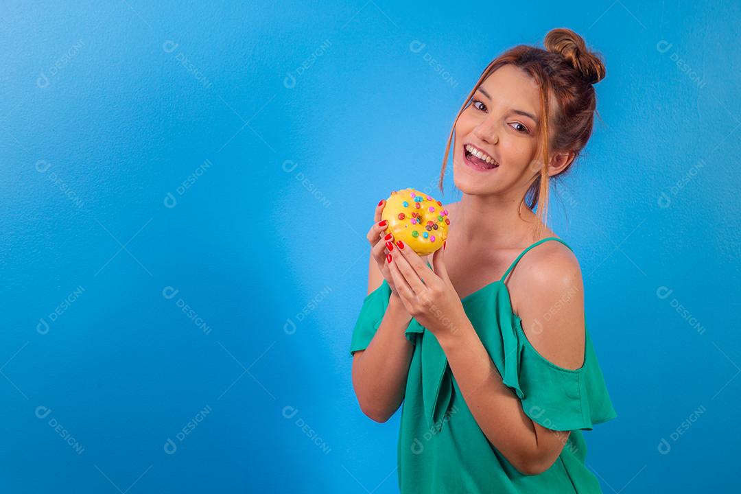 garota ruiva com rosquinha amarela e confetes coloridos sobre fundo azul.