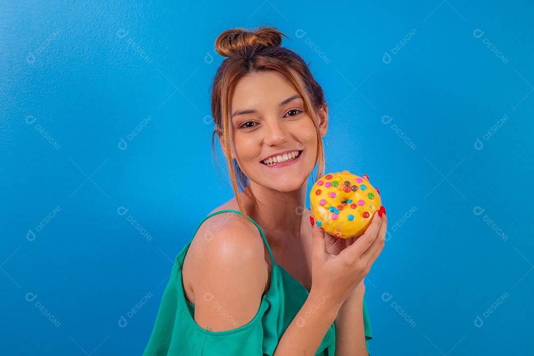 garota ruiva com rosquinha amarela e confetes coloridos sobre fundo azul.