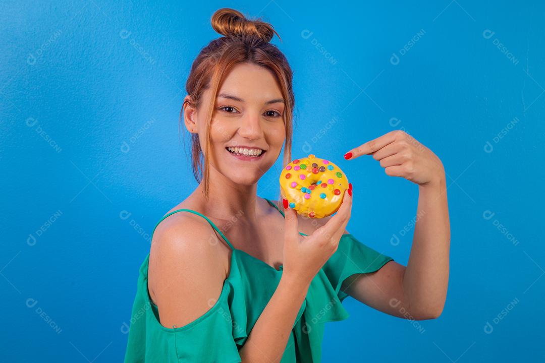 garota ruiva com rosquinha amarela e confetes coloridos sobre fundo azul.