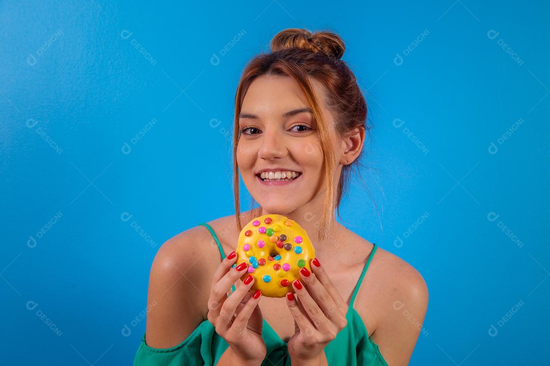 garota ruiva com rosquinha amarela e confetes coloridos sobre fundo azul.