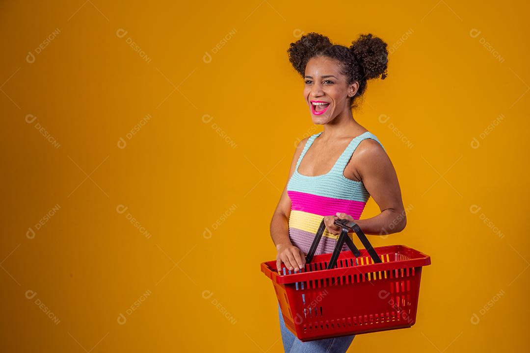Jovem Afro Mulher sorridente segurando cesta de compras vazia