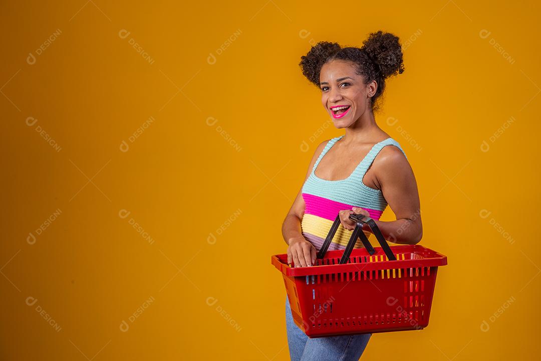 Jovem Afro Mulher sorridente segurando cesta de compras vazia