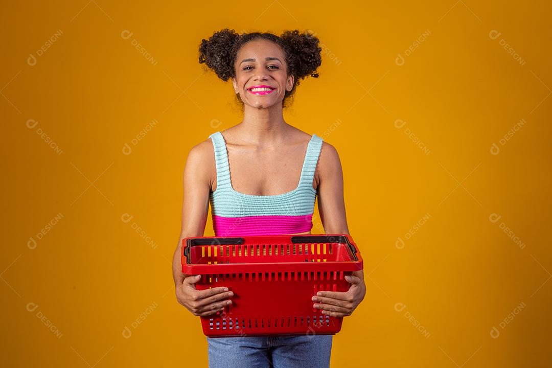 Jovem Afro Mulher sorridente segurando cesta de compras vazia